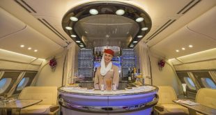 Cabina di prima classe Emirates con hostess sorridente al bar di bordo, simbolo del lusso contrapposto al low cost di Ryanair nella battaglia sui social.