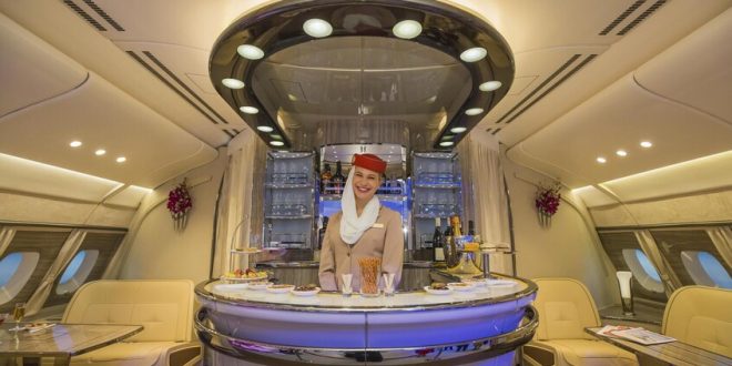 Emirates vs Ryanair: la battaglia sui social tra lusso e ironia 1 Cabina di prima classe Emirates con hostess sorridente al bar di bordo, simbolo del lusso contrapposto al low cost di Ryanair nella battaglia sui social.